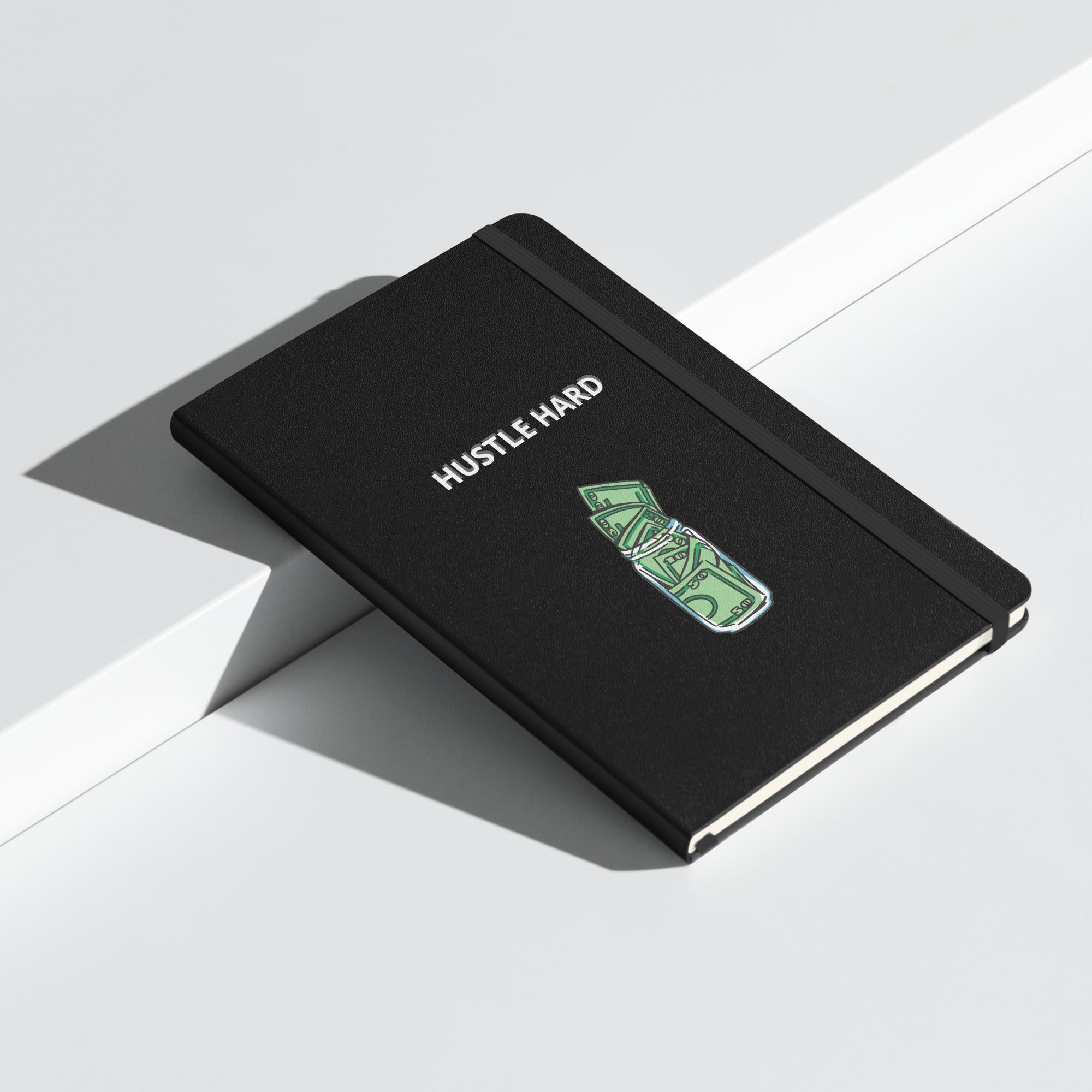 Schwarzes Notizbuch mit weißem Schriftzug „HUSTLE HARD“ und einem grünen Geldschein-Motiv.