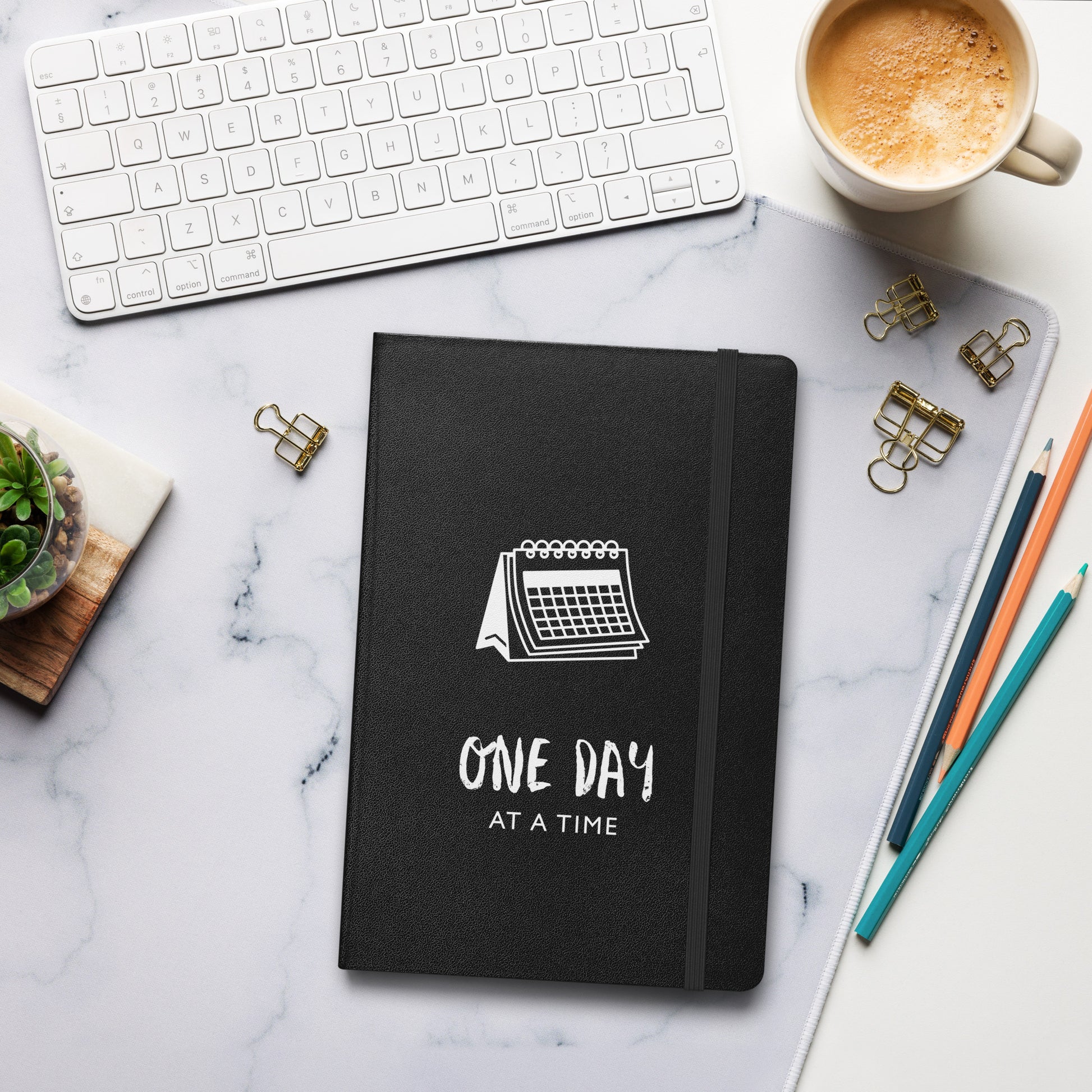Schwarzes Notizbuch mit weißem Kalender-Motiv und dem Text: „One day at a time“
