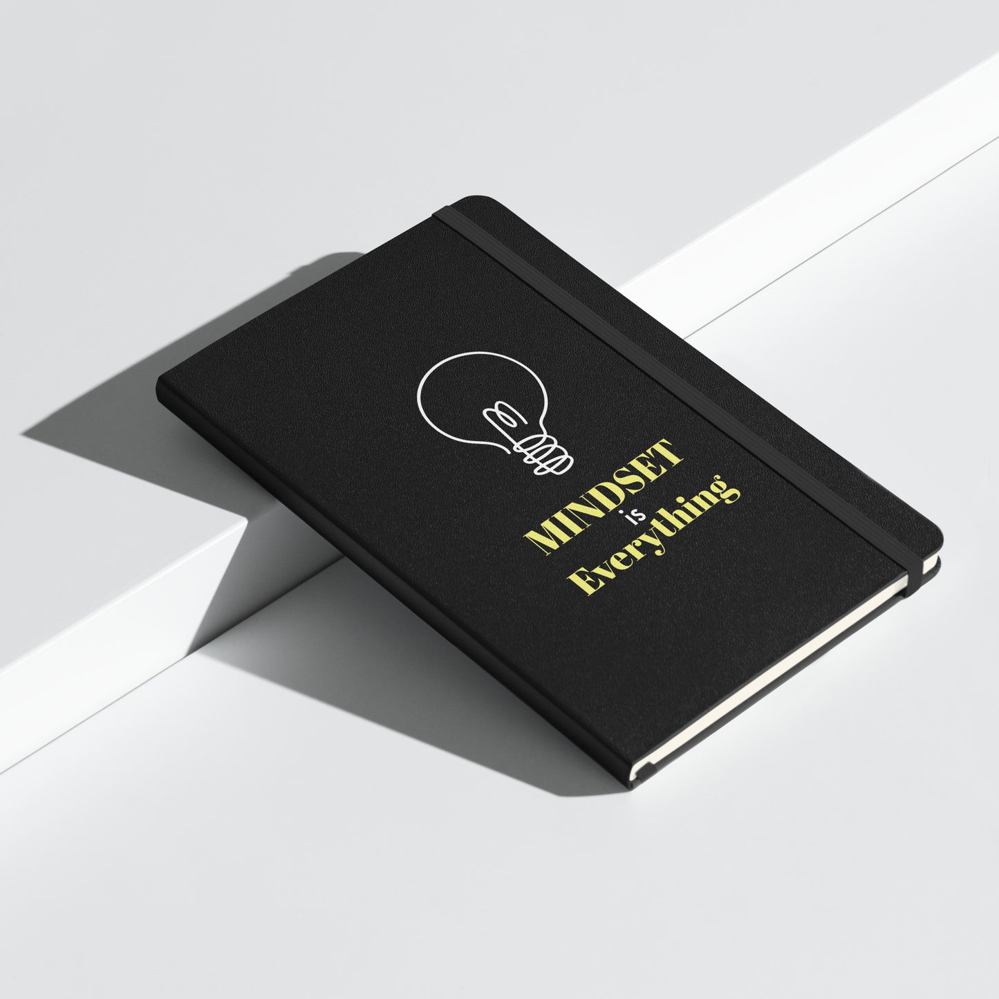 Schwarzes Notizbuch mit gelbem Text: „MINDSET is Everything“ und einer weißen Glühbirnen-Grafik.