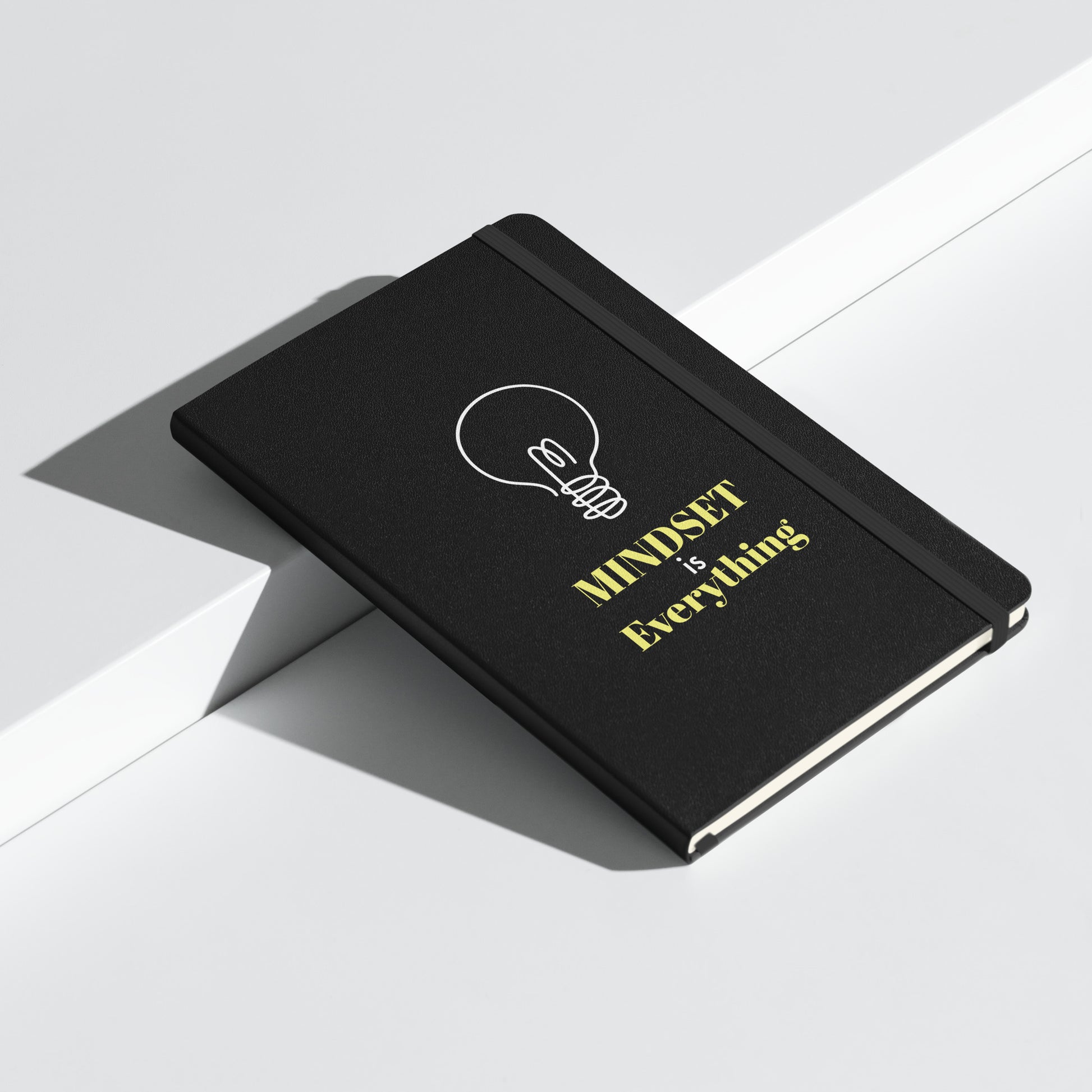 Schwarzes Notizbuch mit gelbem Text: „MINDSET is Everything“ und einer weißen Glühbirnen-Grafik.