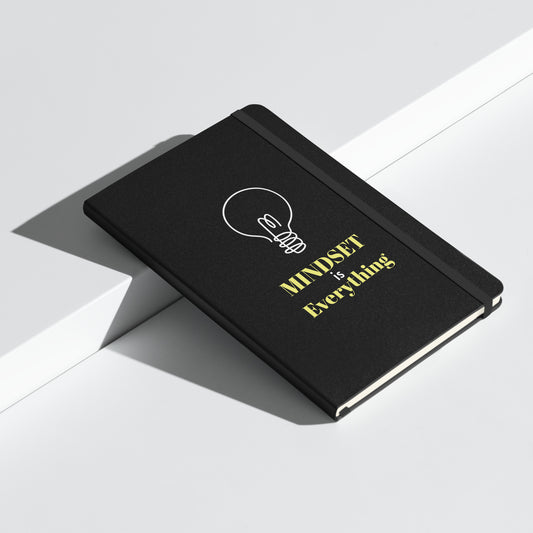 Schwarzes Notizbuch mit gelbem Text: „MINDSET is Everything“ und einer weißen Glühbirnen-Grafik.