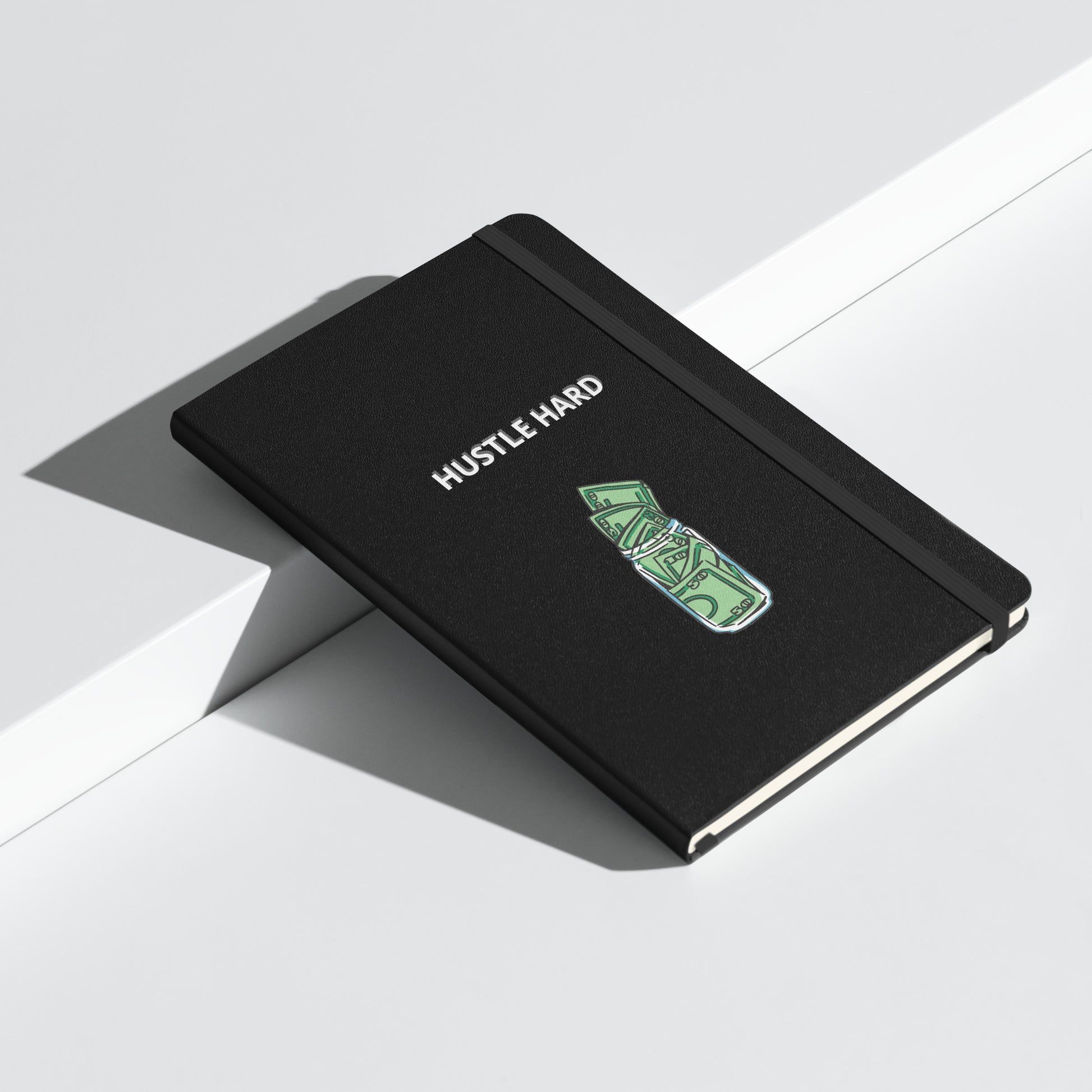 Schwarzes Notizbuch mit weißem Schriftzug „HUSTLE HARD“ und einem grünen Geldschein-Motiv.