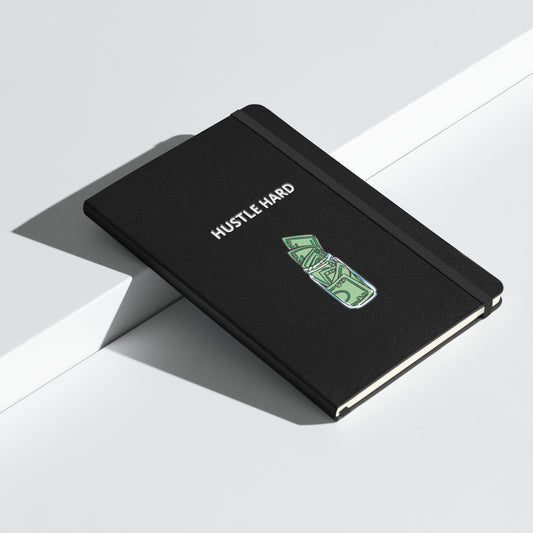 Schwarzes Notizbuch mit weißem Schriftzug „HUSTLE HARD“ und einem grünen Geldschein-Motiv.