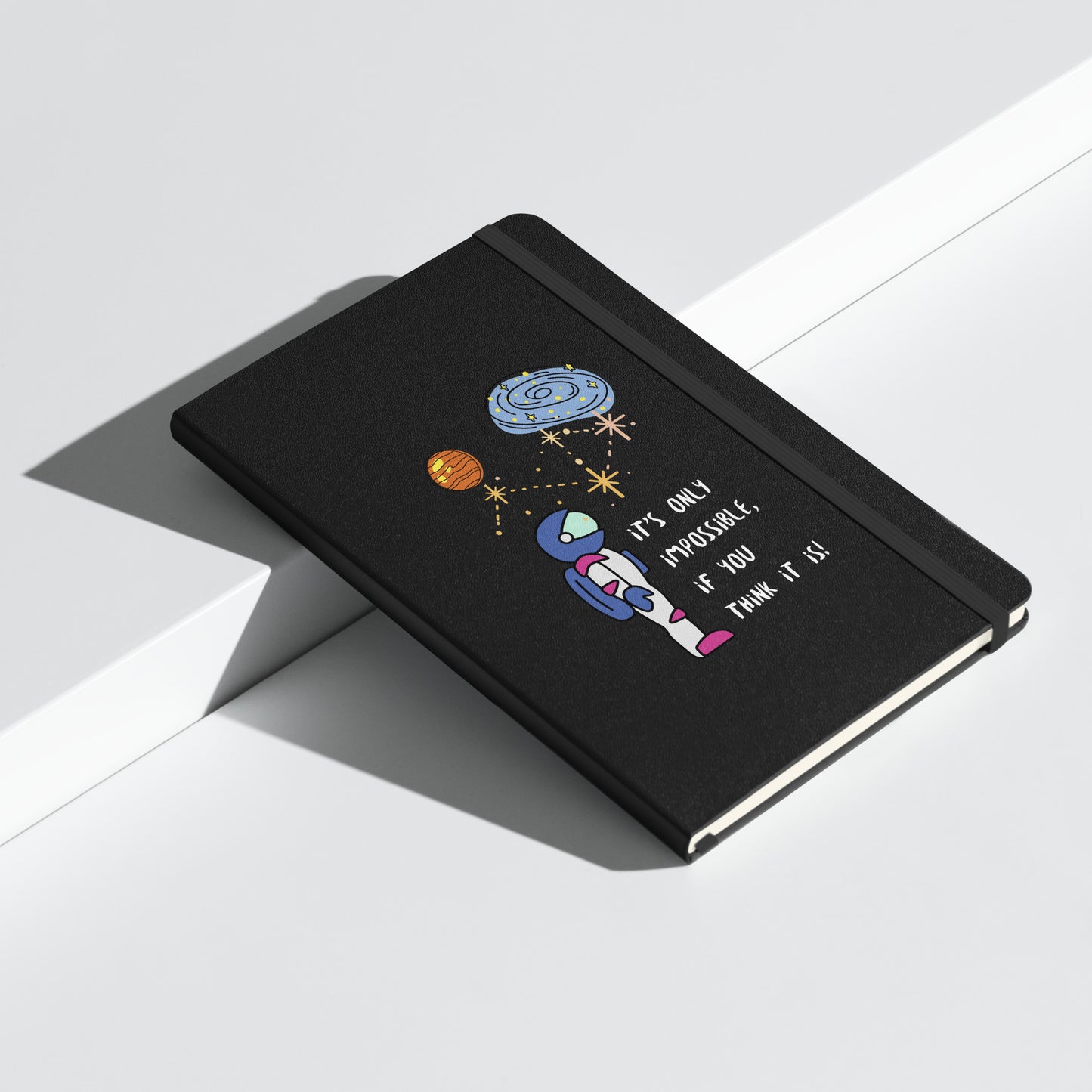 Black notebook with an astronaut illustration, planets, and the quote "It's only impossible if you think it is" on the cover.