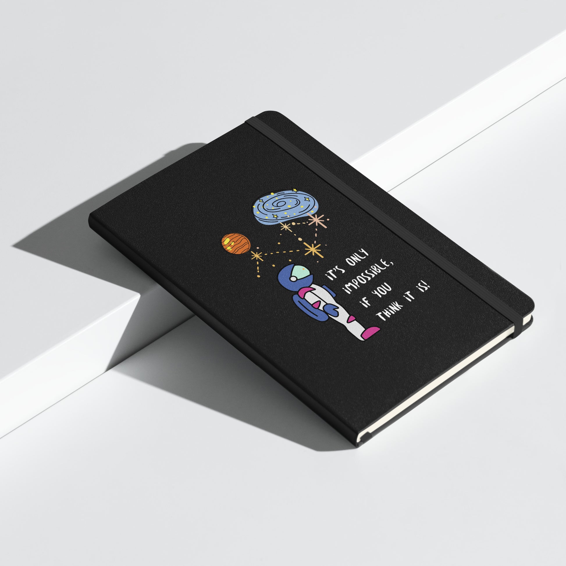 Black notebook with an astronaut illustration, planets, and the quote "It's only impossible if you think it is" on the cover.