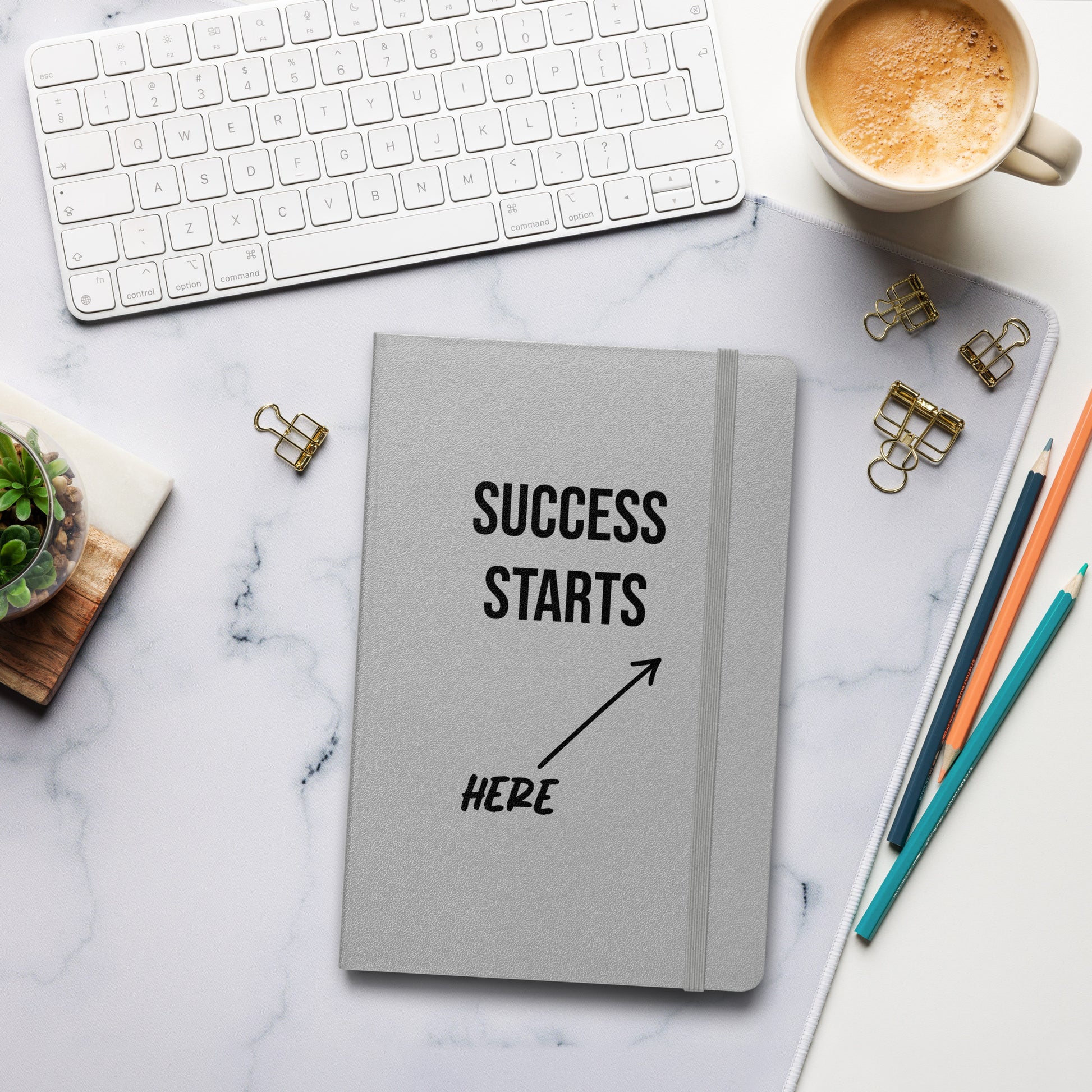 Graues Notizbuch mit schwarzem Text: „SUCCESS STARTS HERE“ und einem Pfeil nach oben.