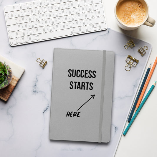 Graues Notizbuch mit schwarzem Text: „SUCCESS STARTS HERE“ und einem Pfeil nach oben.