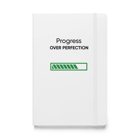 Weißes Notizbuch mit dem Text: „Progress over perfection“ und einem grünen Fortschrittsbalken.