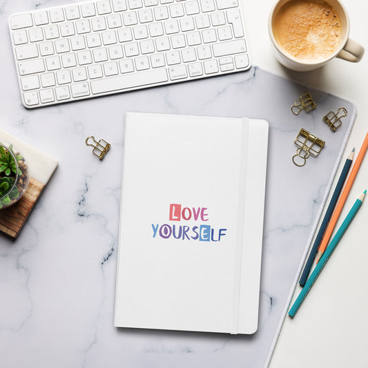 White notebook with colorful "Love Yourself" text on the cover.